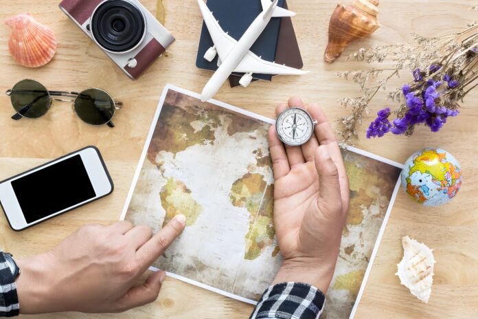 Mains posées sur une carte du monde avec une boussole, entourées d'un smartphone, d'un appareil photo et d'un avion miniature